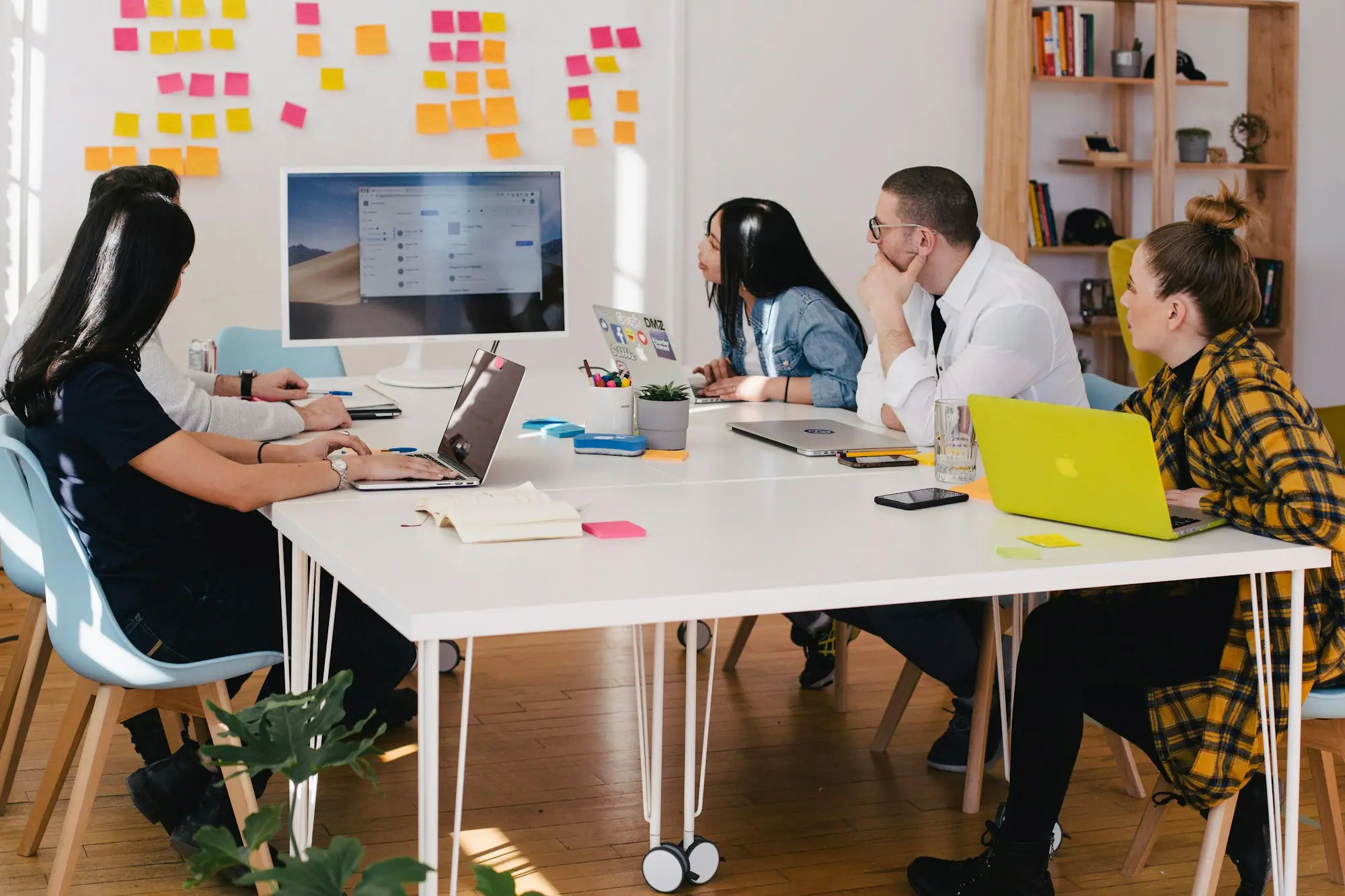 Equipo de trabajo reunido alrededor de una mesa blanca con laptops en una oficina luminosa