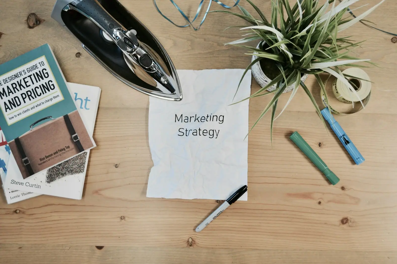 Hoja con el título «Marketing Strategy» sobre un escritorio junto a un libro y una planta