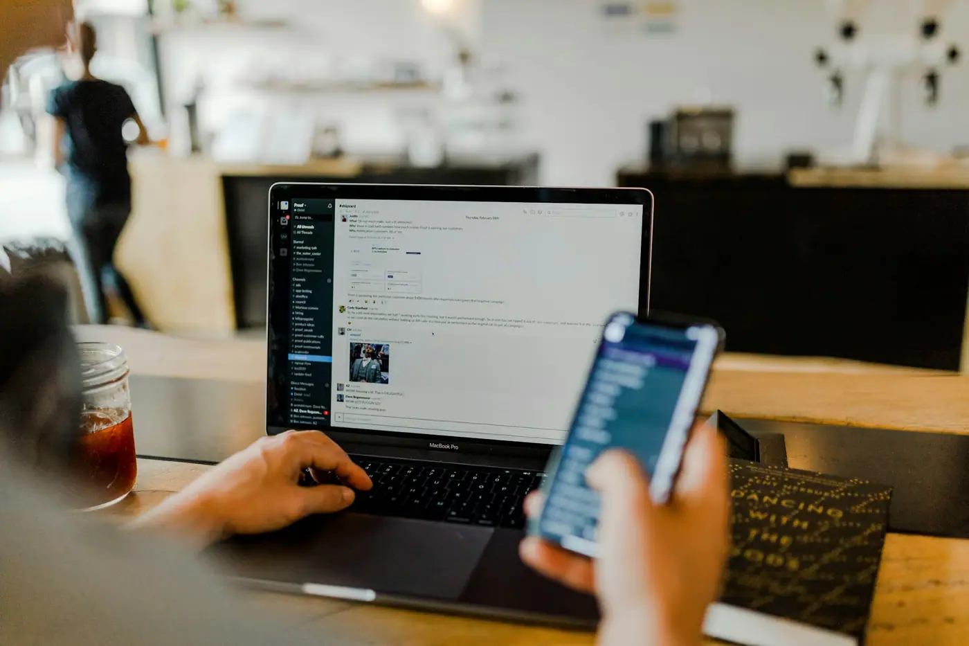 Manos sosteniendo un celular con un feed de redes sociales junto a una laptop